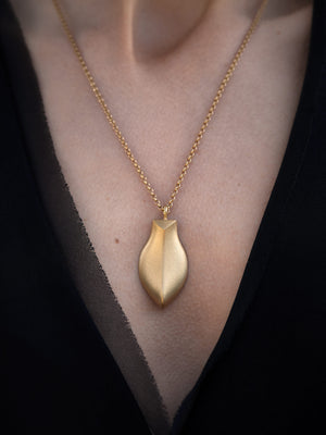 Large sculptural gold pendant worn with black v neck top