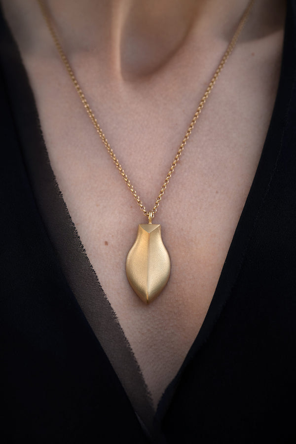 Large sculptural gold pendant worn with black v neck top