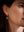 A close-up side profile of a woman wearing a small silver-toned drop earring with a rectangular gray stone pendant against a dark background.
